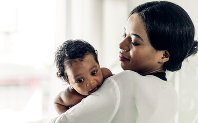Portrait of enjoy happy love family african american mother playing with adorable little african american baby.Mom kiss with cute son moments good time in a white bedroom.Love of black family