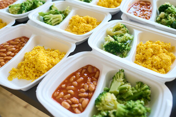 Part of table served with steamed broccoli, kasha and boiled beans in white plastic containers...
