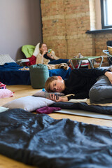 Schoolboy with mobile phone resting on sleeping place on the floor and texting against young female...