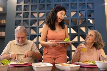 Família brasileira jantando. Mãe conversando feliz com avós