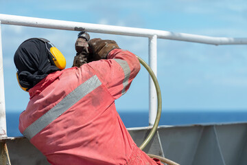 Seaman ship crew working on deck derusting the vessel for painting.