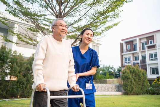 Asian young caregiver nurse support senior older male walking outdoors. 