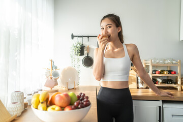 Asian attractive active woman holding red apple in kitchen at home. 
