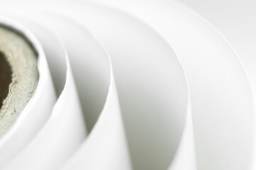 Fototapeta premium Blurred white polygraph paper on a cardboard spool. A bundle of leftover paper in a printing house. Material for the printing industry. Close-up, top view, defocused