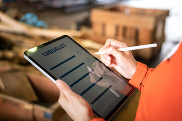 Action of a human is using digital pen to perform checklist on tablet with background of factory...