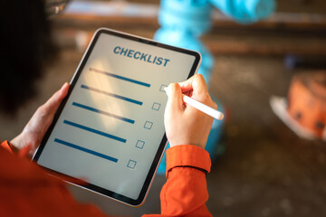 Action of a human is using digital pen to checking checklist on tablet with background of factory workplace. Industrial and technology working concept. Close-up and selective focus at hand's part.