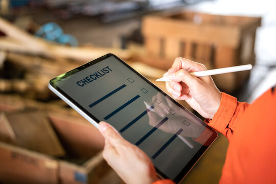 Action of a engineer is using digital pen to checking checklist on tablet with background of factory workplace. Industrial and technology working concept. Close-up and selective focus at hand's part.