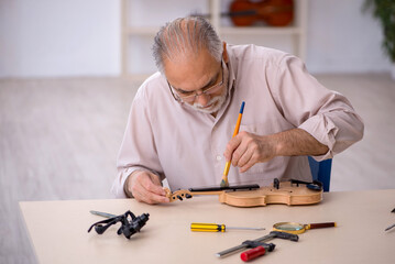 Old male repairman repairing musical instruments at workshop
