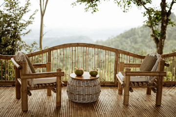 Couple chairs on balcony of countryside bamboo terrace  house with mountain view background in the morning. Two coconuts on the table, couple vacation concept