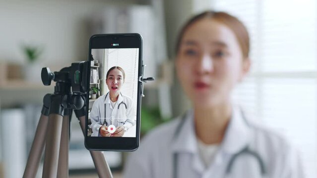 Asian woman doctor making online live streaming broadcast talking over camera recording in hospital, medical and healthcare blogger, vlogger concept