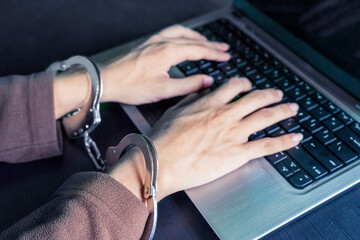 Hacker hands handcuffed using a laptop on table