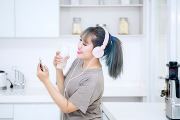 Happy woman enjoying music while drink in kitchen
