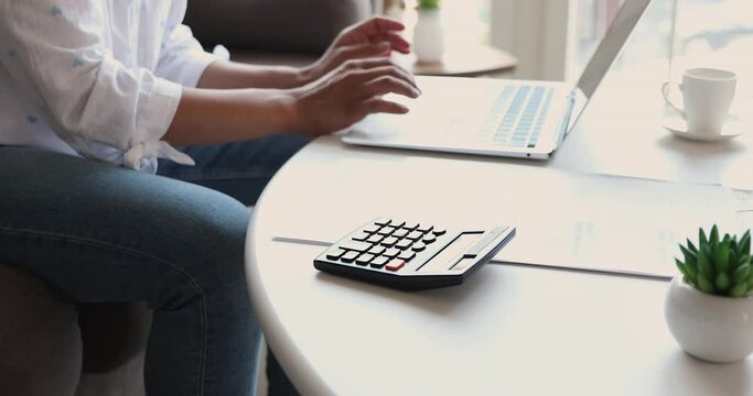 Close up of young woman hands type on laptop and digital calculator check sum of utility bills before make payment online in ebank app. Millennial female balance domestic budget prepare to pay taxes