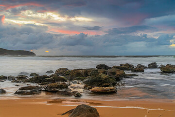 Soft sunrise seascape with rocks and rain clouds