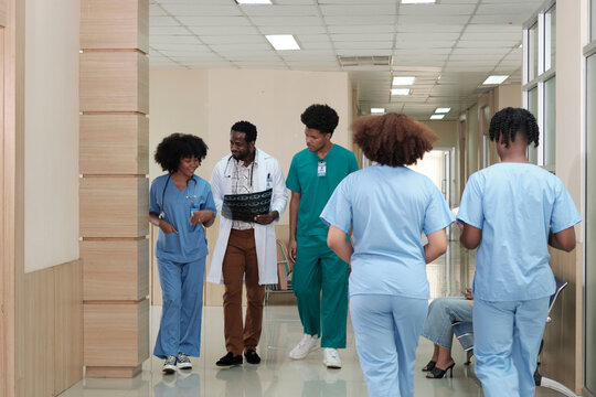 Group of practitioners, professional African American male doctor with young medical students team happy walk and discuss diagnosis X-ray film at examination outpatient healthcare clinic in hospital.