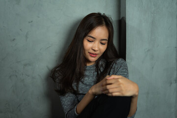Fototapeta premium Young woman sitting against wall, hug knee, depression emotion, looking down in dark room, Portrait of young beautiful woman or female or girl sitting expression depression emotional alone