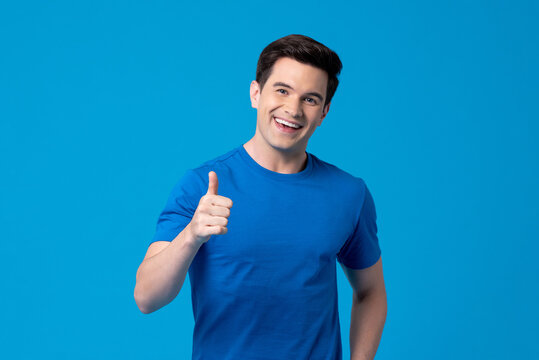Smiling handsome young Caucasian man giving thumbs up in light blue isolated background