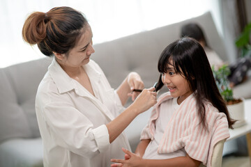 Asian Mother cutting hair to her daughter in living room at home while stay at home safe from Covid-19 Coronavirus during lockdown. Self-quarantine and social distancing concept.