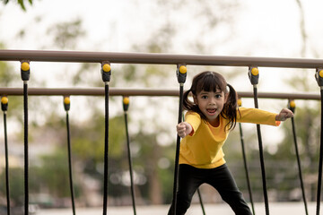 Fototapeta premium summer, childhood, leisure and people concept - happy little girl on children playground climbing frame