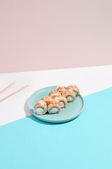 Maki roll with shrimp on ceramic plate with chopsticks. Shrimp sushi roll with philadelphia cheese on coloured background. Japanese menu concept. Prawn sushi roll in modern style.