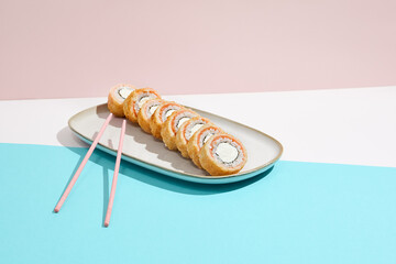 Baked Philadelphia Maki with salmon on ceramic plate. Hot tempura sushi with salmon and philadelphia cheese on coloured background. Japanese menu concept. Hot maki sushi in modern style.