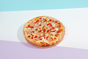 Italian pizza with ham and pickled cucumber on coloured background. Meat pizza with ham and vegetables in minimal style on light blue color. American pizza delivery concept with color backdrop