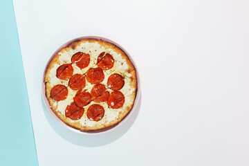 Italian pizza with pepperoni and cheese on coloured background. Cheese focaccia with salami in minimal style on blue and orange color. American pizza delivery concept with color backdrop