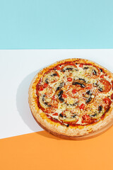 Italian pizza with mushroom and cheese on coloured background. Vegan pizza with mushroom and tomato in minimal style on blue and orange color. American pizza delivery concept with color backdrop