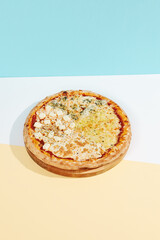 Italian pizza with four cheese on coloured background. Quattro formaggi pizza in minimal style on blue and orange color. American pizza delivery concept with color backdrop