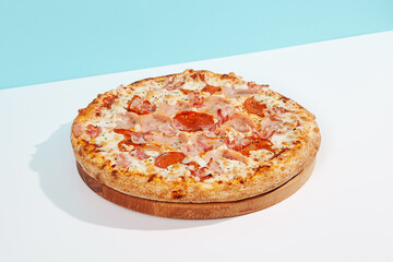 Italian pizza with ham and bacon on coloured background. Meat pizza with bacon and ham in minimal style on blue and orange color. American pizza delivery concept with color backdrop