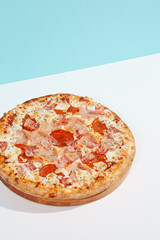 Italian pizza with ham and bacon on coloured background. Meat pizza with bacon and ham in minimal style on blue and orange color. American pizza delivery concept with color backdrop