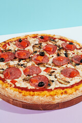 Italian pizza with salami, mushroom, black olives on coloured background. Meat pizza with salami and olives minimal style on blue and purple color. American pizza delivery concept with color backdrop