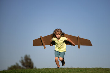 Child playing with cardboard toy wings in the park. Concept of children day. Kid boy in an pilot...