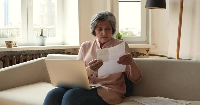 Busy Hispanic woman retiree sit on sofa read paper document bill check financial data online use laptop satisfied with rational spending money. Older lady focused on paperwork manage utility payments