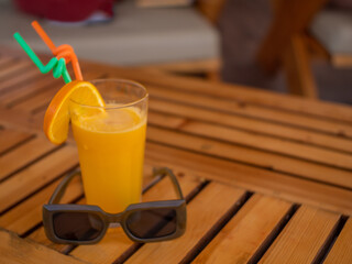 Composition of a glass of orange juice and sunglasses on the table.