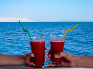 Two female hands hold glasses with fruit cocktails on the background of the sea.