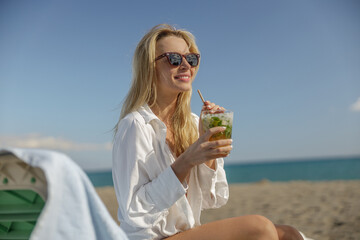 Happy lady in sunglasses chilling with mohito cocktail on sunny beach