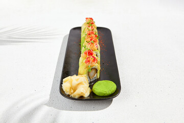 Modern asian food - sushi roll with avocado and tuna on black plate on white concrete background.  Maki roll with avocado outside, tempura shrimp inside in minimal style. Fusion sushi menu.