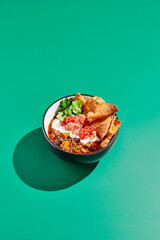 Chili con carne on colour background with hard shadow. Mexican chili in minimal style on green table. Traditional mexican cuisine on trendy design. Chili soup in bowl contemporary concept.