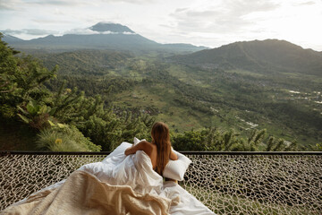 Young woman covering a white blanket sit in hammock  at the view of nature of mountains with green...