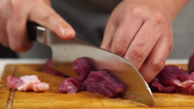 Close-up of a cook carving red meat with a chef's knife on a kitchen board. Slow motion. Front view. Cutting fresh meat in a home kitchen