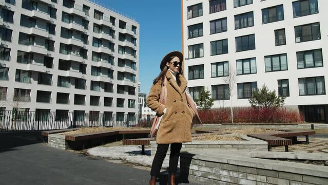 A girl with glasses against the background of a modern house. Blue sky and beige clothes on a young woman.