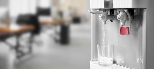 Pouring of fresh water from modern cooler into glass in office, closeup