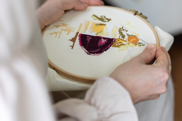 Cross-stitch embroidering in progress. Young girl in linen clothes is doing handmade embroidery