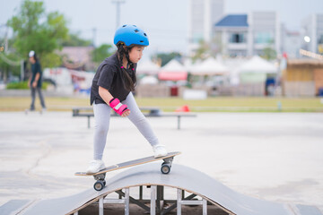 Child or kid girl playing surfskate or skateboard in skating rink or sports park at parking to wearing safety helmet elbow pads wrist and knee support - 503399052