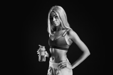 Black and white portrait of sporty young African-American woman with bottle of water on dark...