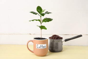 Cup with coffee tree and pot of beans on table