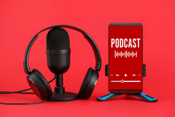 Microphone, headphones and mobile phone with word PODCAST on screen on red background
