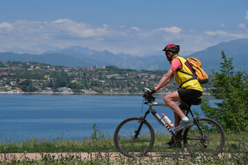 A man on a bike ride along the lake. Man cycling along Lake Garda with the Alps in the background.