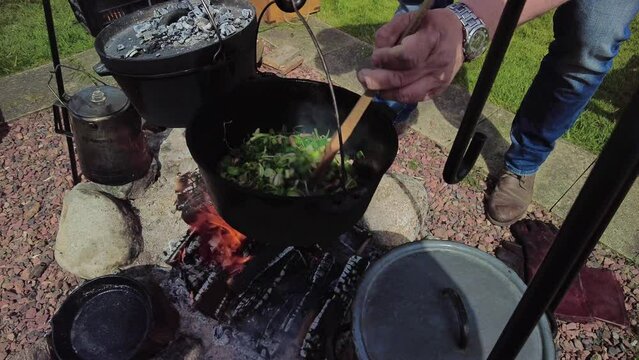 Cooking on the campfire, cooking on a crackling campfire, stirring in a cast iron pan with freshly cut vegetables